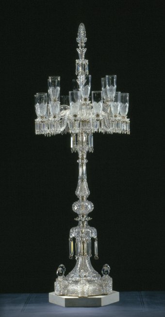 Fig. 43: Candelabrum with 18 candle arms, blown, cut; white marble plinth. F. & C. Osler (design no. 2811), about 1883. H. 295 cm. The Corning Museum of Glass, Corning, New York (96.2.10). The original design, dated June 1881, had six kerosene lamps, but Osler adapted it for candles in October 1883. It was later made for electricity as well.